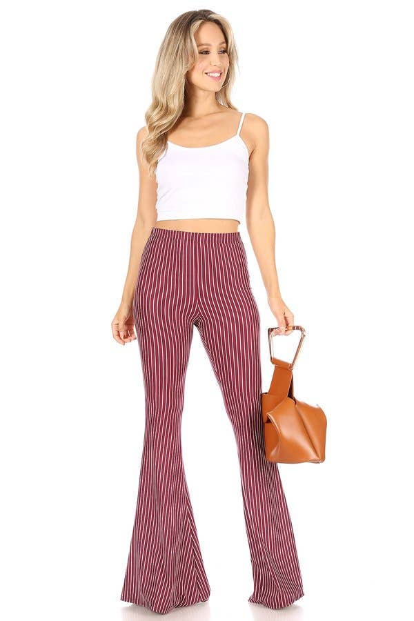 model wearing high-waisted, flared pants with vertical red and ivory stripes. Styled with white crop top and geometric brown handbag.