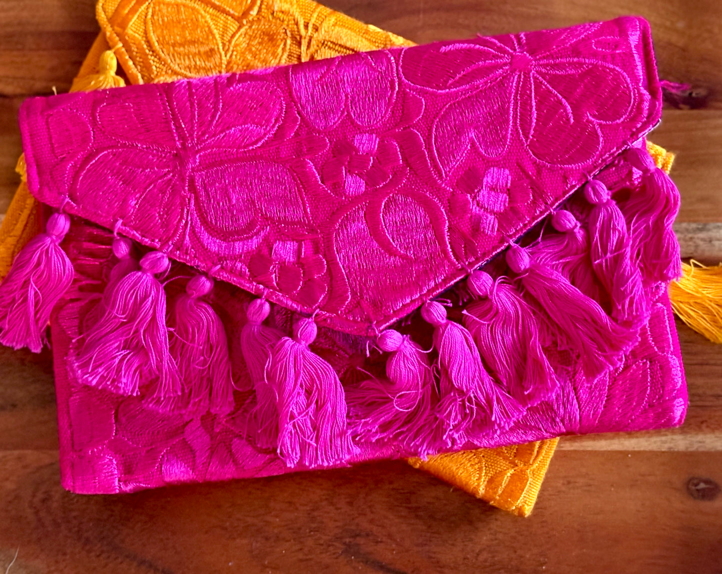 Pink embroidered clutch with tassels on a wooden surface