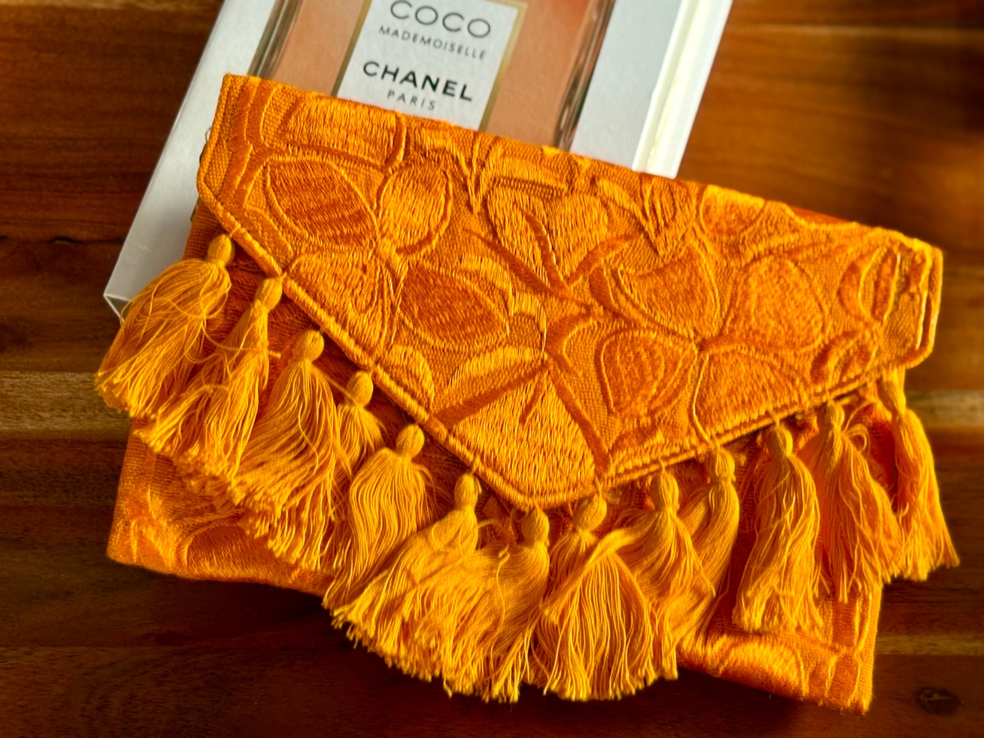 Yellow clutch with tassels in front of a Chanel perfume bottle