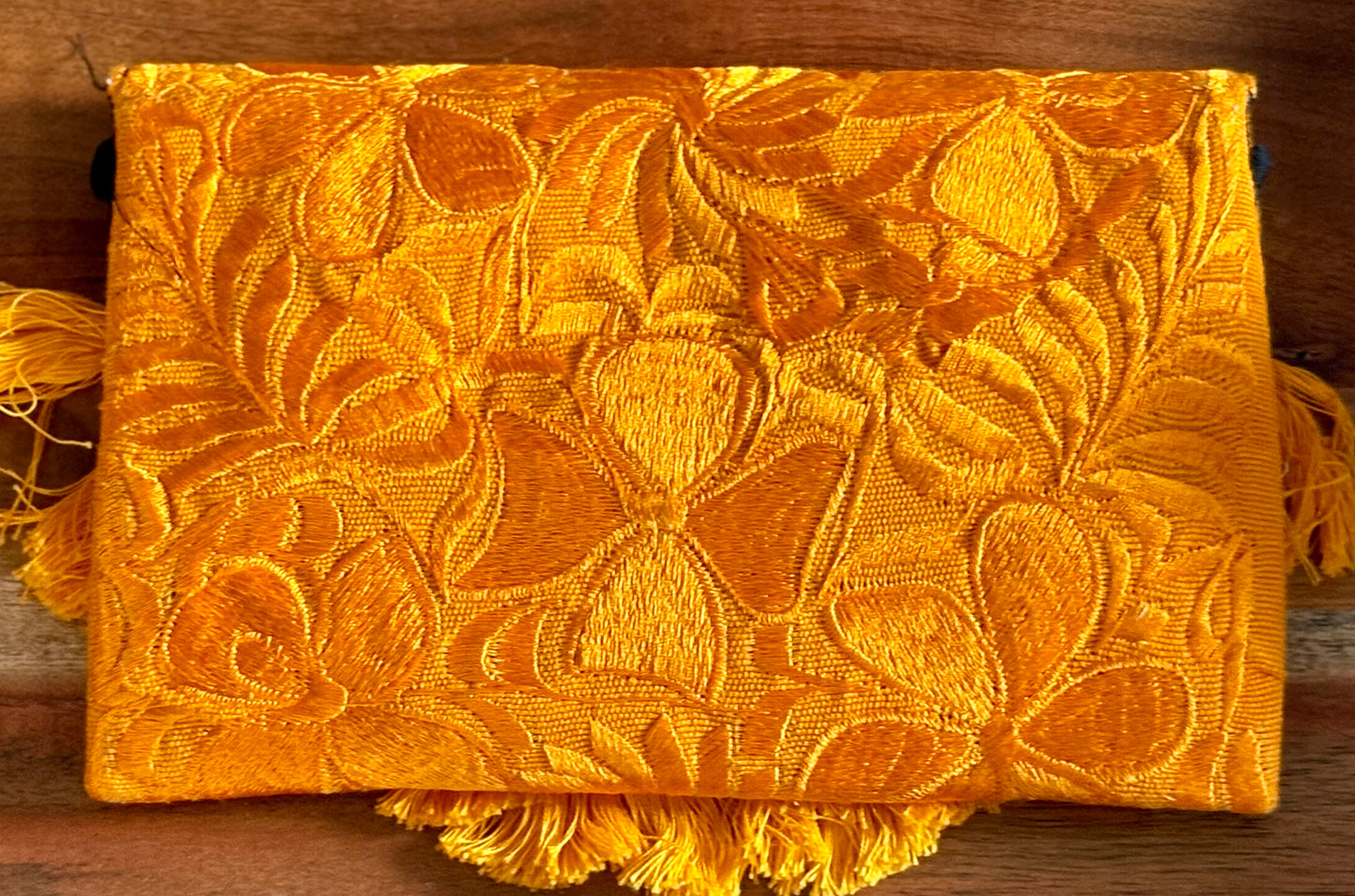 Yellow textured fabric with leaf patterns and tassels on a wooden surface