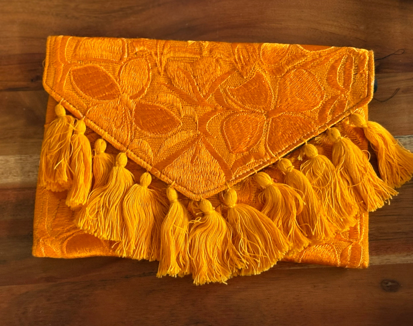 Yellow clutch bag with tassels on a wooden surface