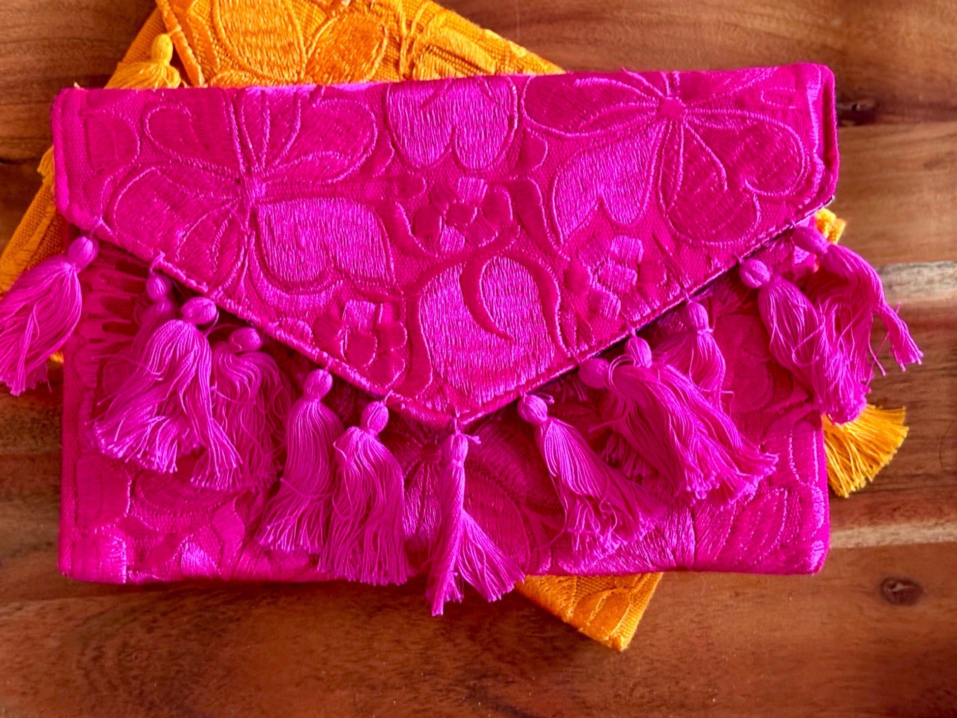 Pink clutch bag with tassels on a wooden surface