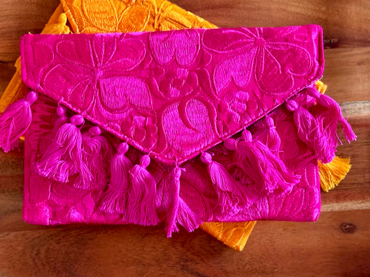 Pink clutch bag with tassels on a wooden surface