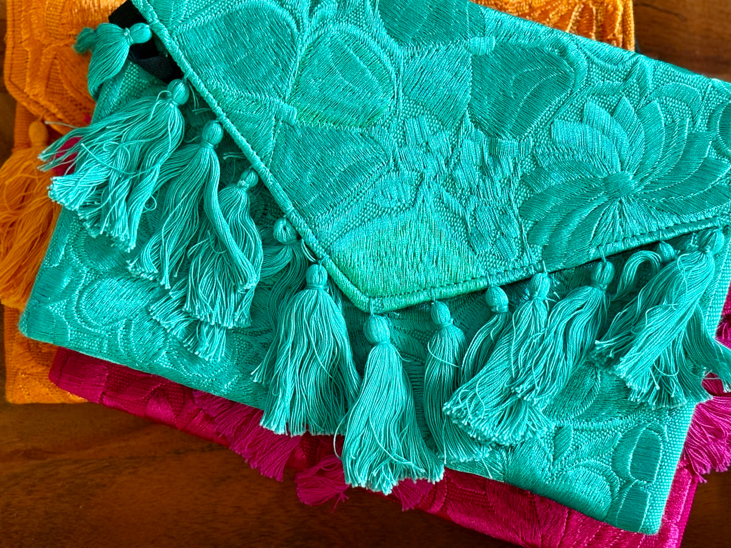 Turquoise embroidered clutch with tassels on a wooden surface