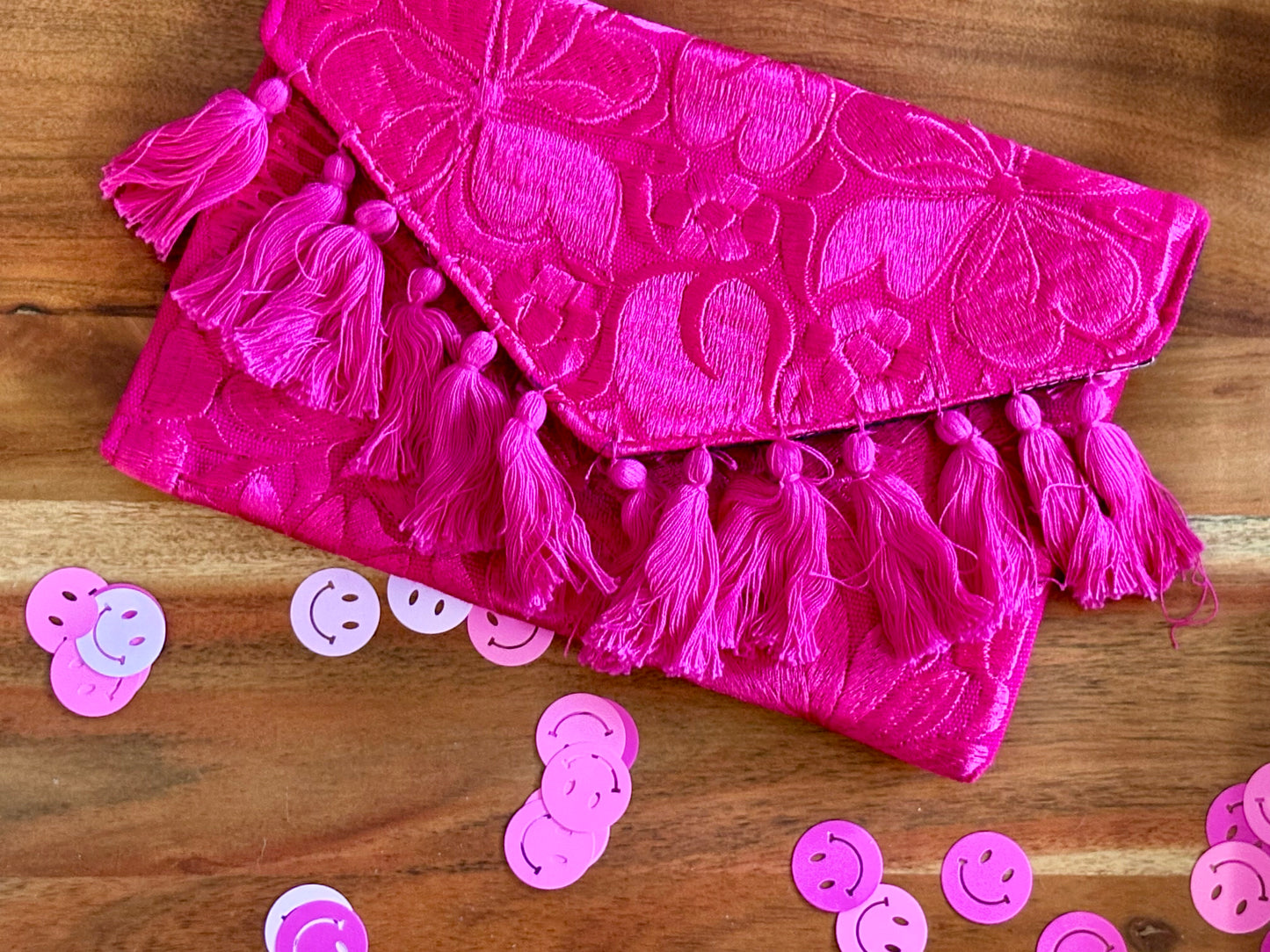Pink clutch bag with tassels on a wooden surface with pink confetti.
